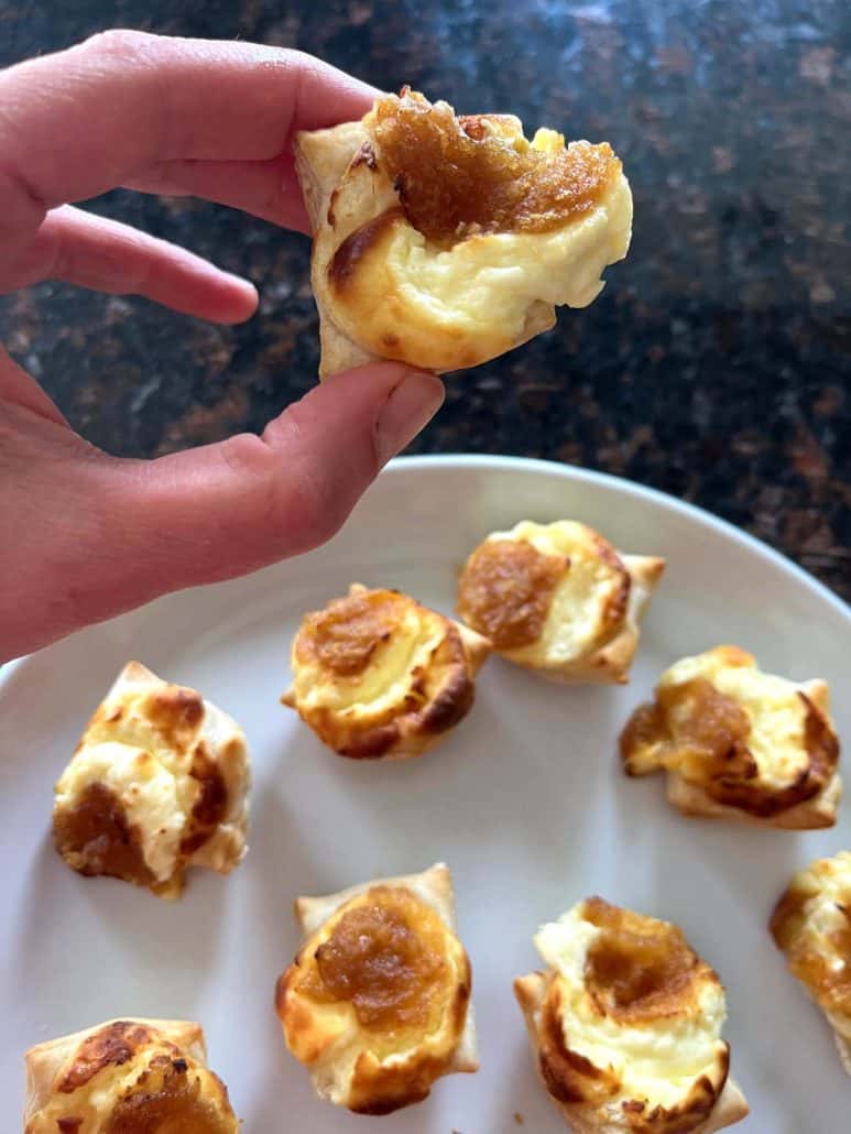 Hand holding an air fried Trader Joe’s Pastry Bite with melted cheese visible inside, plate of bites in the background.