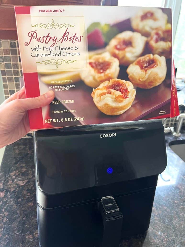 Holding a box of Trader Joe’s Pastry Bites in front of the air fryer before cooking, ready to make a quick and crispy appetizer.