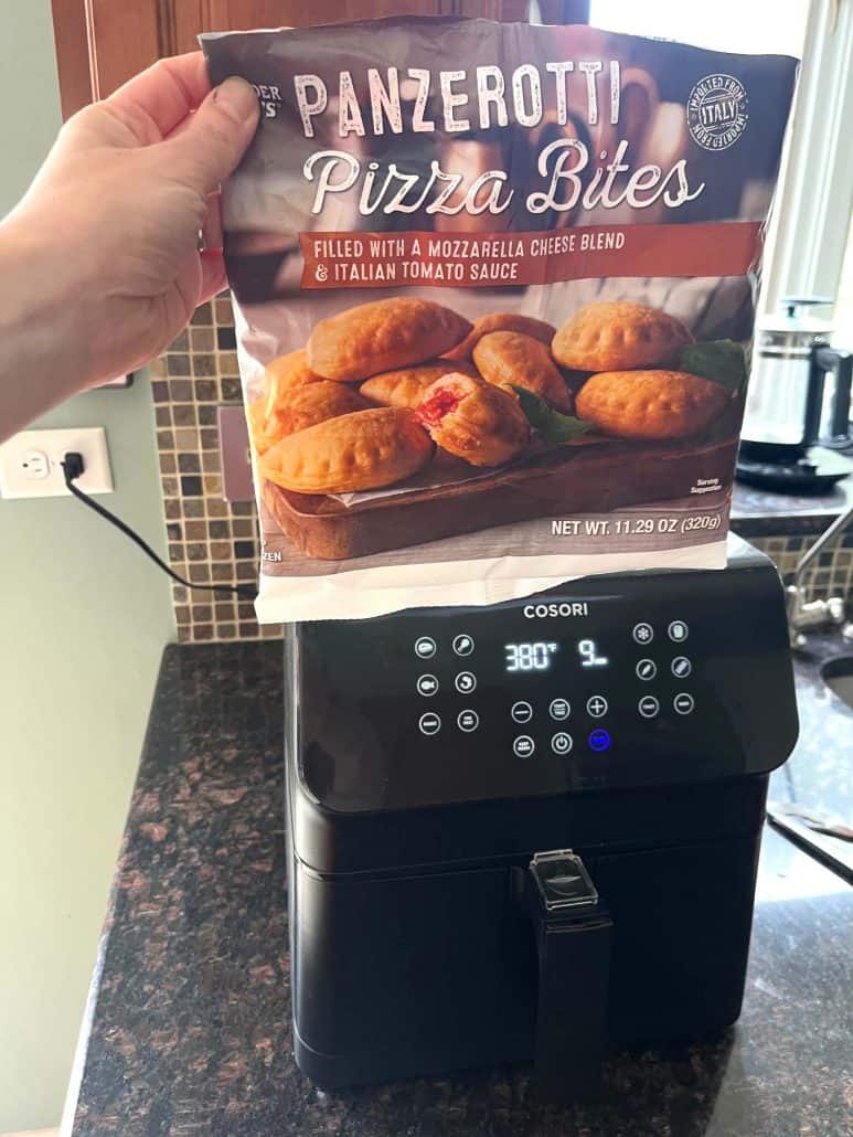 Hand holding a bag of Trader Joe’s Panzerotti Pizza Bites above an air fryer, just before cooking.