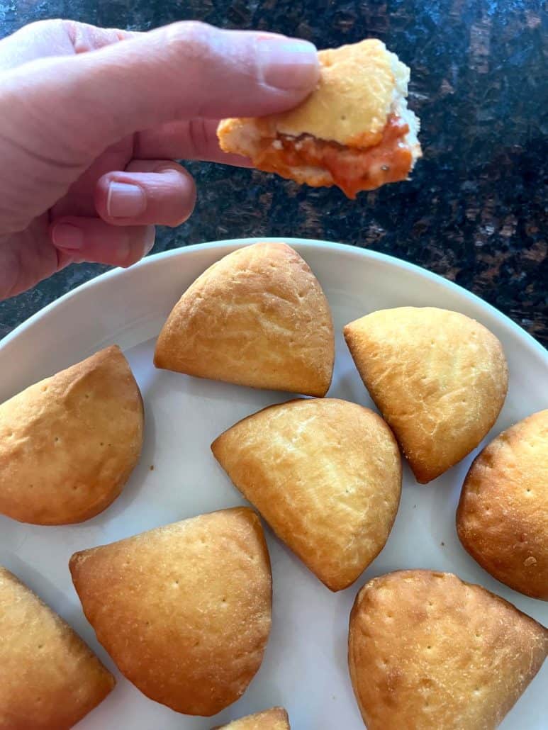 Hand holding a bitten Trader Joe’s Panzerotti Pizza Bite showing gooey cheese and tomato sauce filling—highlighting the delicious results of this air fryer recipe.