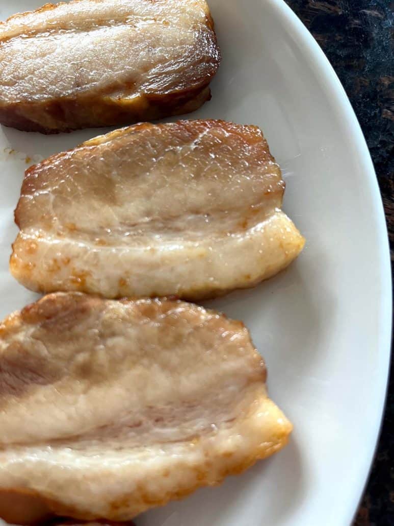 Air-fried Trader Joe’s pork belly slices on a white plate—crispy, golden, and ready to serve.