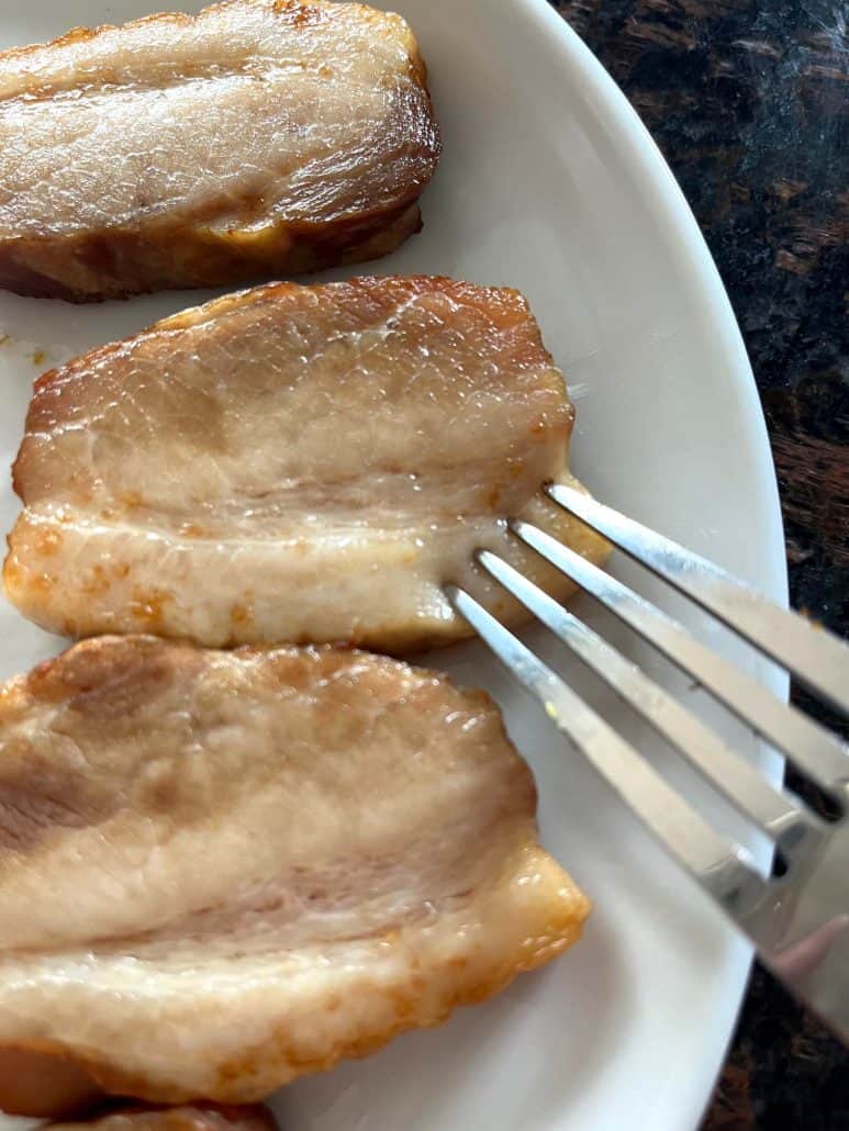 Fork slicing into a crispy piece of air-fried Trader Joe’s pork belly on a white plate—showing the tender texture from the 9-minute air fryer method.