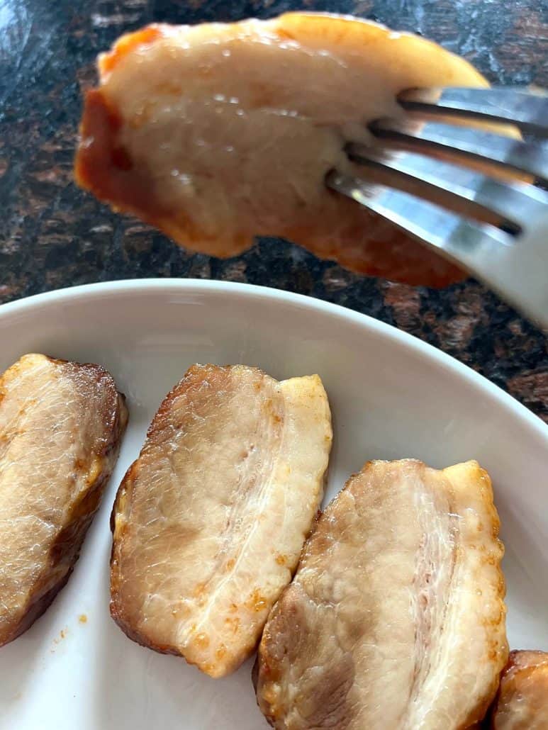 Fork holding a tender slice of crispy air-fried Trader Joe’s pork belly above a plate, ready to enjoy.