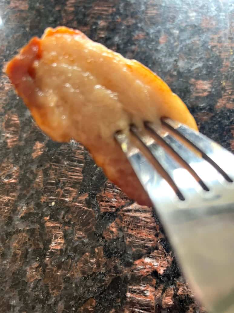 Close-up of a juicy, crispy slice of Trader Joe’s pork belly held on a fork, fresh out of the air fryer and ready to eat.