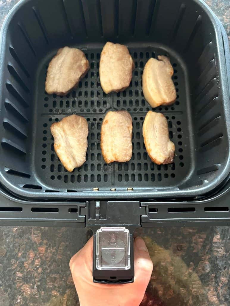 Air fryer basket with six Trader Joe’s pork belly slices cooking in a single layer—perfectly arranged for even crisping during the 9-minute air fryer recipe.