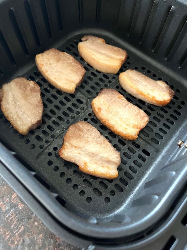Cooked Trader Joe’s pork belly slices inside the air fryer basket, perfectly browned and crisp after 9 minutes.