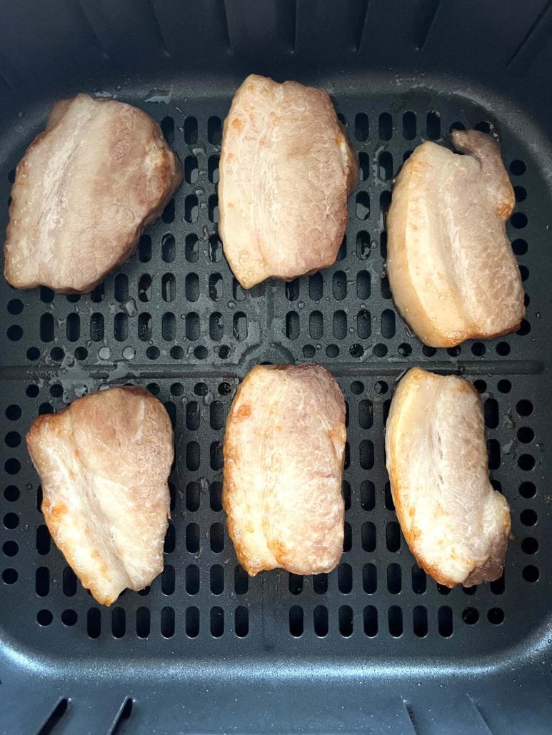 Slices of Trader Joe’s pork belly arranged in a single layer inside the air fryer basket.
