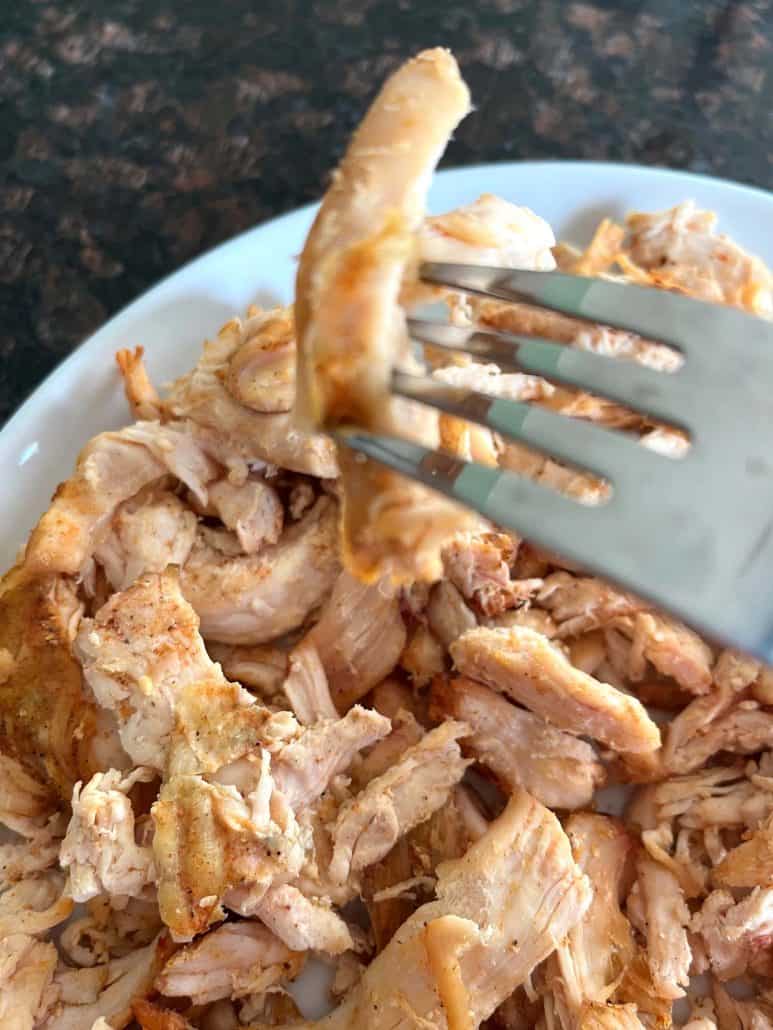 Fork holding a crispy bite of air-fried Trader Joe’s pulled chicken above a plate, highlighting the browned edges and tender texture.