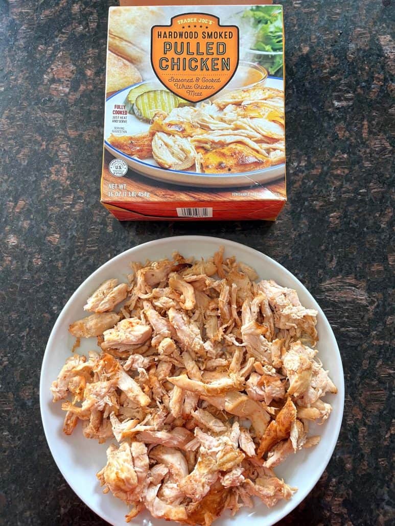 Cooked Trader Joe’s pulled chicken served on a white plate with the product box displayed behind.