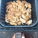 Air fryer basket filled with shredded Trader Joe’s pulled chicken, ready to cook for a quick and easy meal.