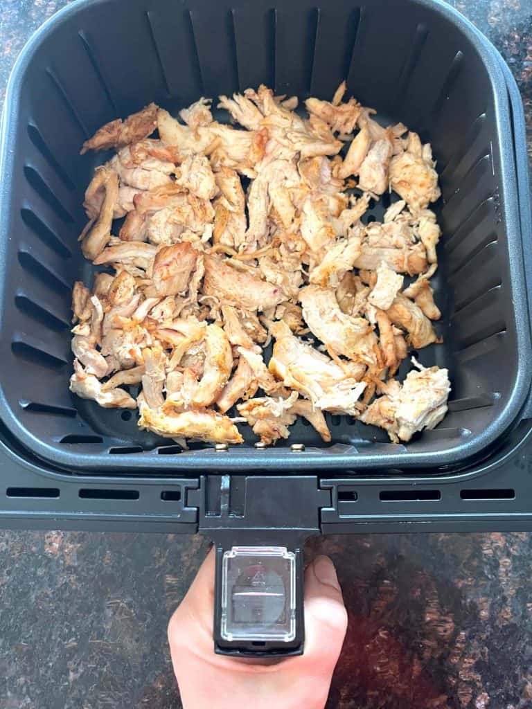 Air fryer basket filled with shredded Trader Joe’s pulled chicken, ready to cook for a quick and easy meal.