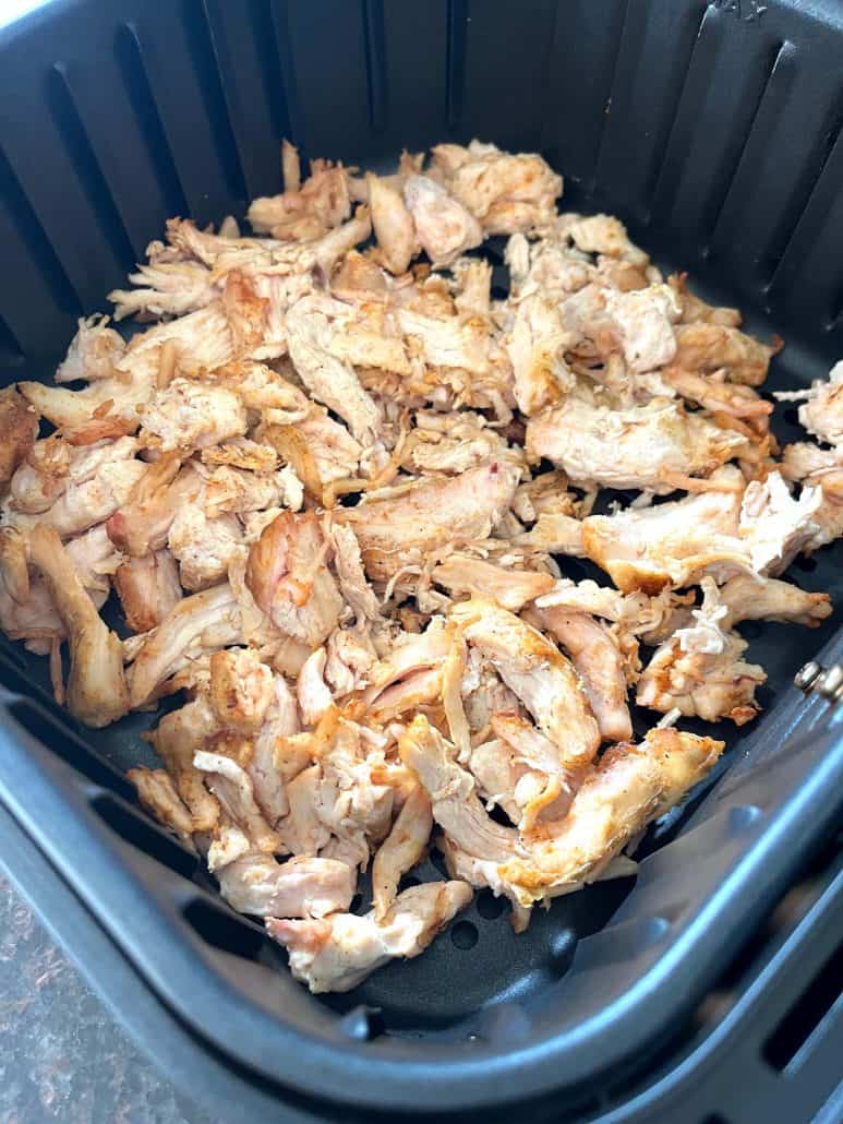 Cooked Trader Joe’s pulled chicken in an air fryer basket, showing its crispy, browned edges after air frying.