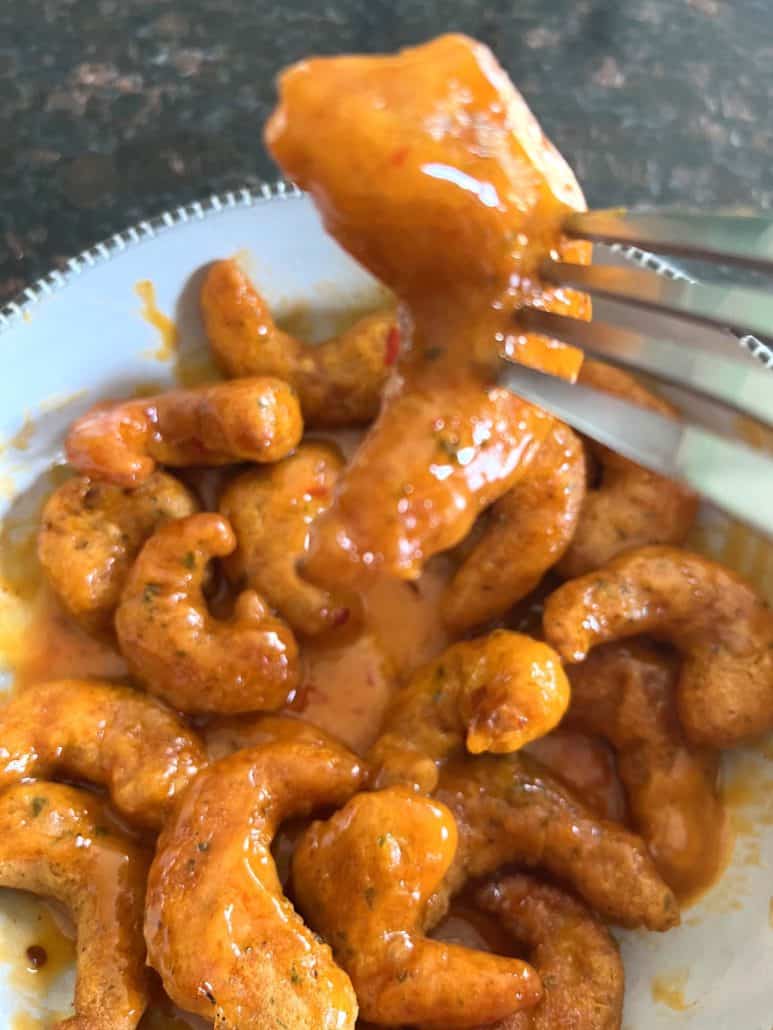 Fork holding saucy Trader Joe’s Shrimp Boom Bah above a bowl—air-fried shrimp coated in sweet and spicy sauce.