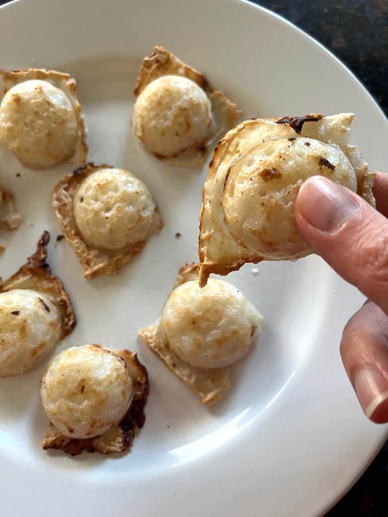 Hand holding a freshly cooked Trader Joe’s Thai Coconut Pancake (Kanom Krok) over a plate of more pancakes—showing the crispy texture and perfect bite-size of this easy air fryer treat.