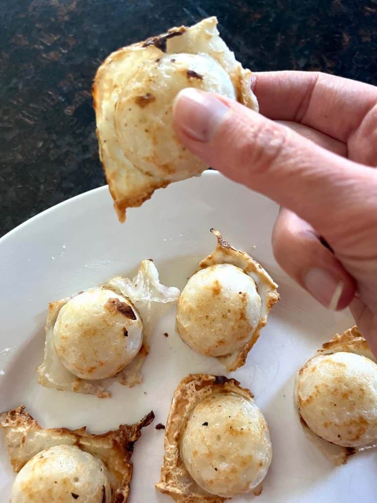Hand holding an air-fried Trader Joe’s Thai Coconut Pancake (Kanom Krok) with a gooey coconut center, showing the creamy inside and crispy edge.