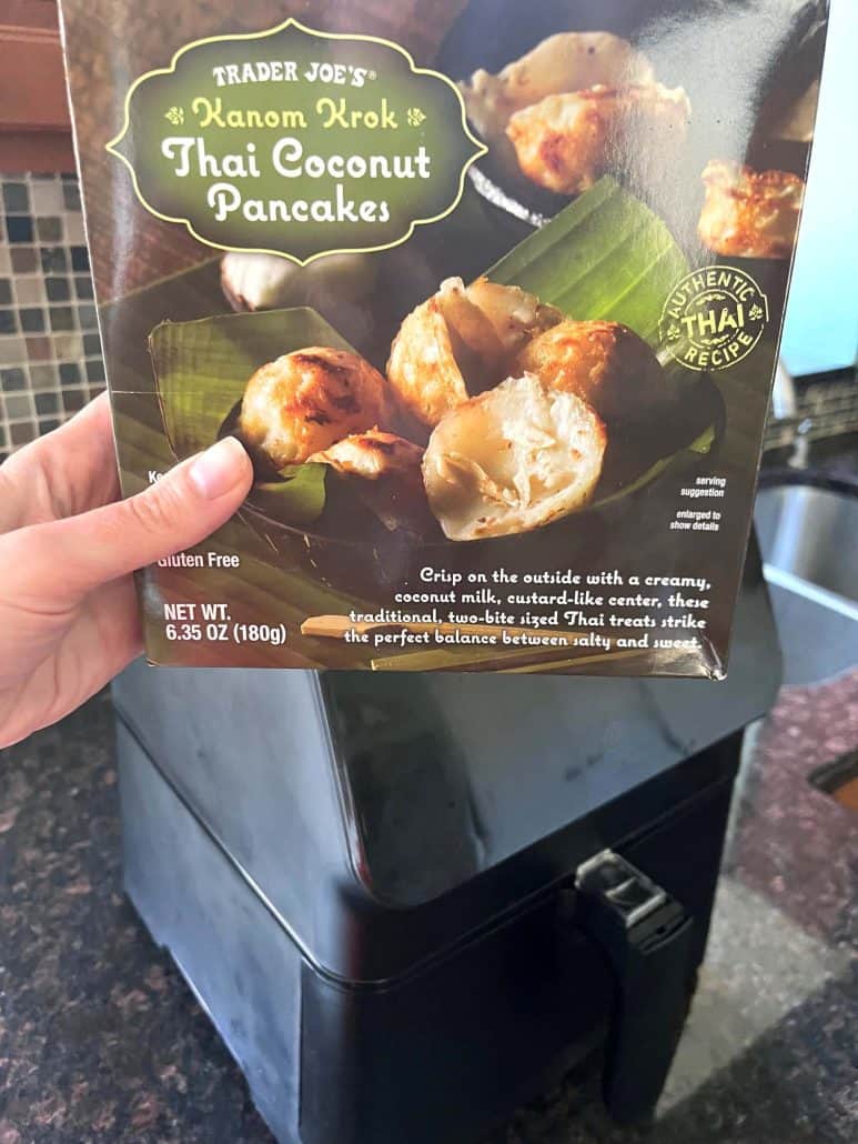 Holding a box of Trader Joe’s Thai Coconut Pancakes (Kanom Krok) in front of an air fryer—getting ready to make this quick and easy frozen dessert recipe.