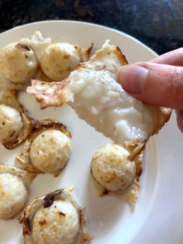Close-up of a hand holding a Trader Joe’s Thai Coconut Pancake (Kanom Krok) with a bite taken out, revealing the creamy coconut filling—highlighting the soft, sweet center of this easy air fryer dessert.