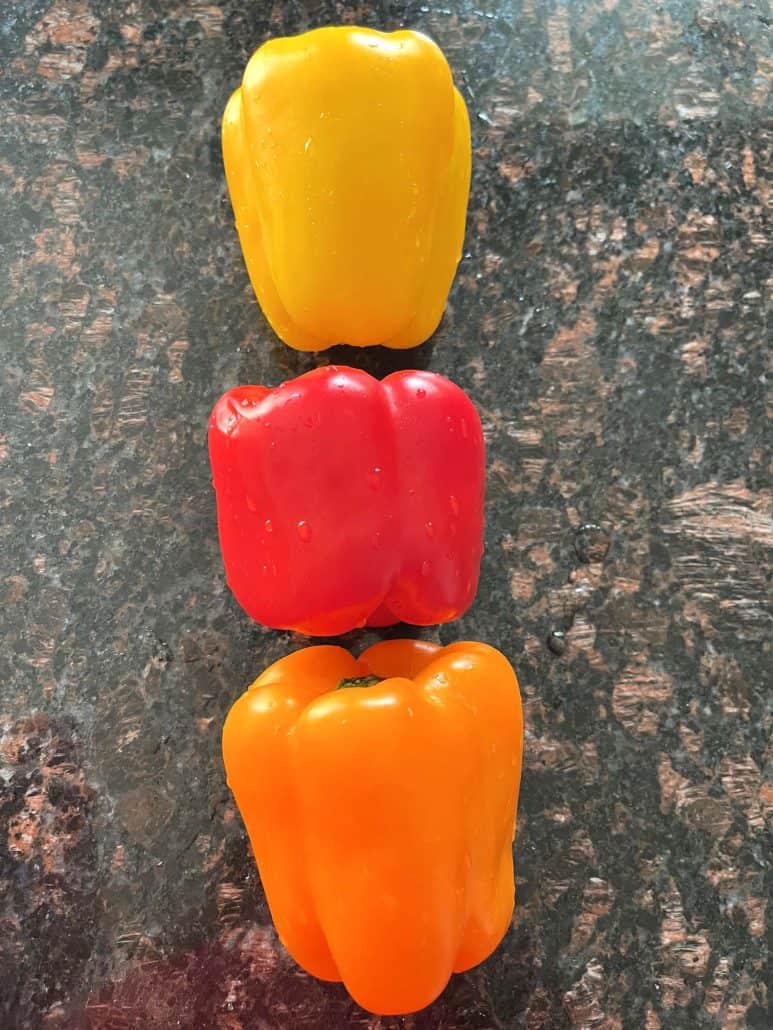 Whole yellow, red, and orange bell peppers lined up on a countertop—these vibrant tri-color peppers are used in the Air Fryer Tri-Color Rainbow Bell Peppers recipe.