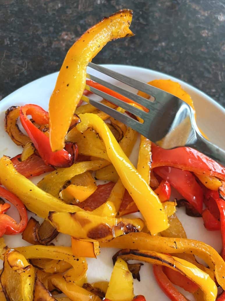 Fork lifting a slice of golden roasted bell pepper from a plate of tri-color peppers—capturing the texture and flavor.
