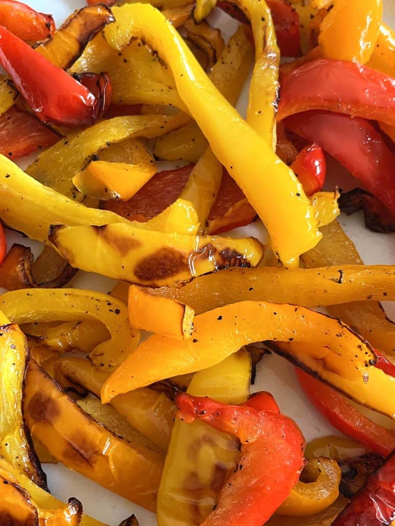 Close-up of roasted red, yellow, and orange bell pepper strips on a plate—highlighting the caramelized edges.