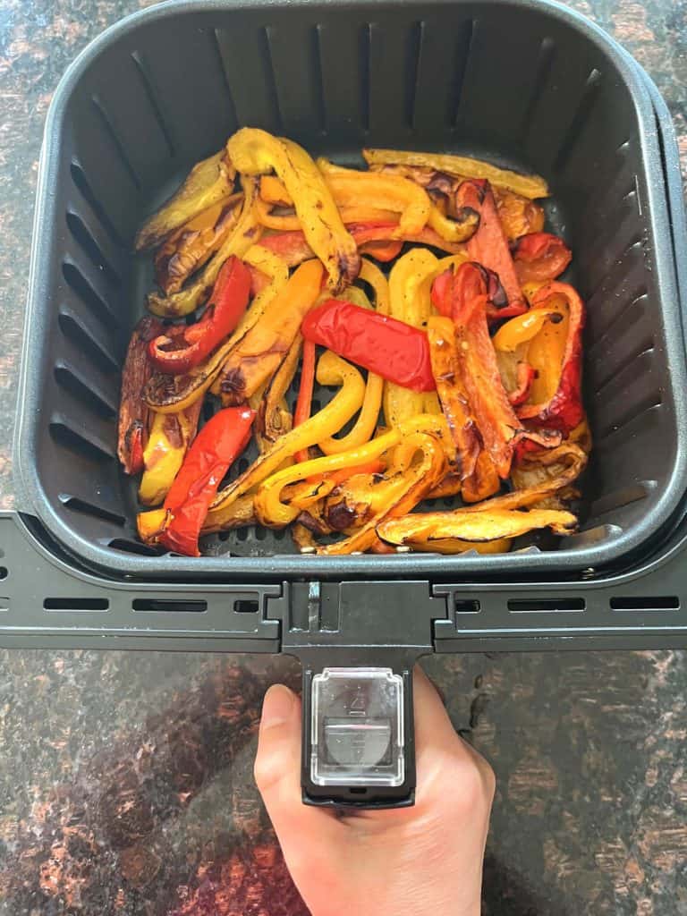 Colorful red, yellow, and orange bell pepper strips freshly roasted in an air fryer basket—perfectly cooked and ready to serve.