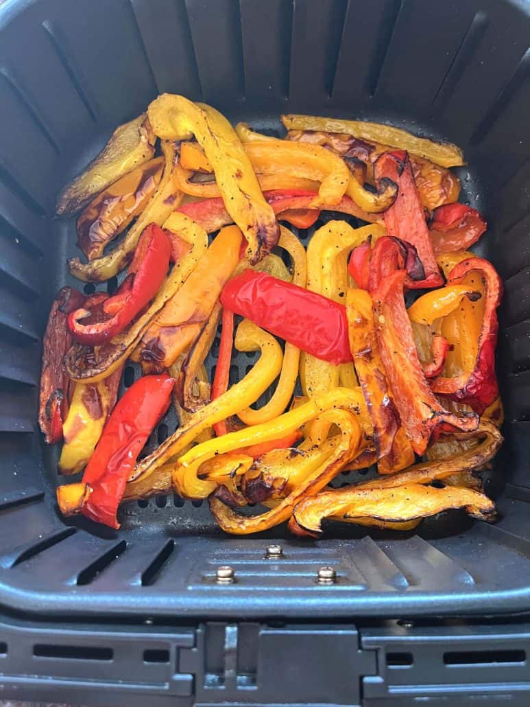 Air fryer basket filled with golden roasted red, yellow, and orange bell pepper strips—perfectly cooked.