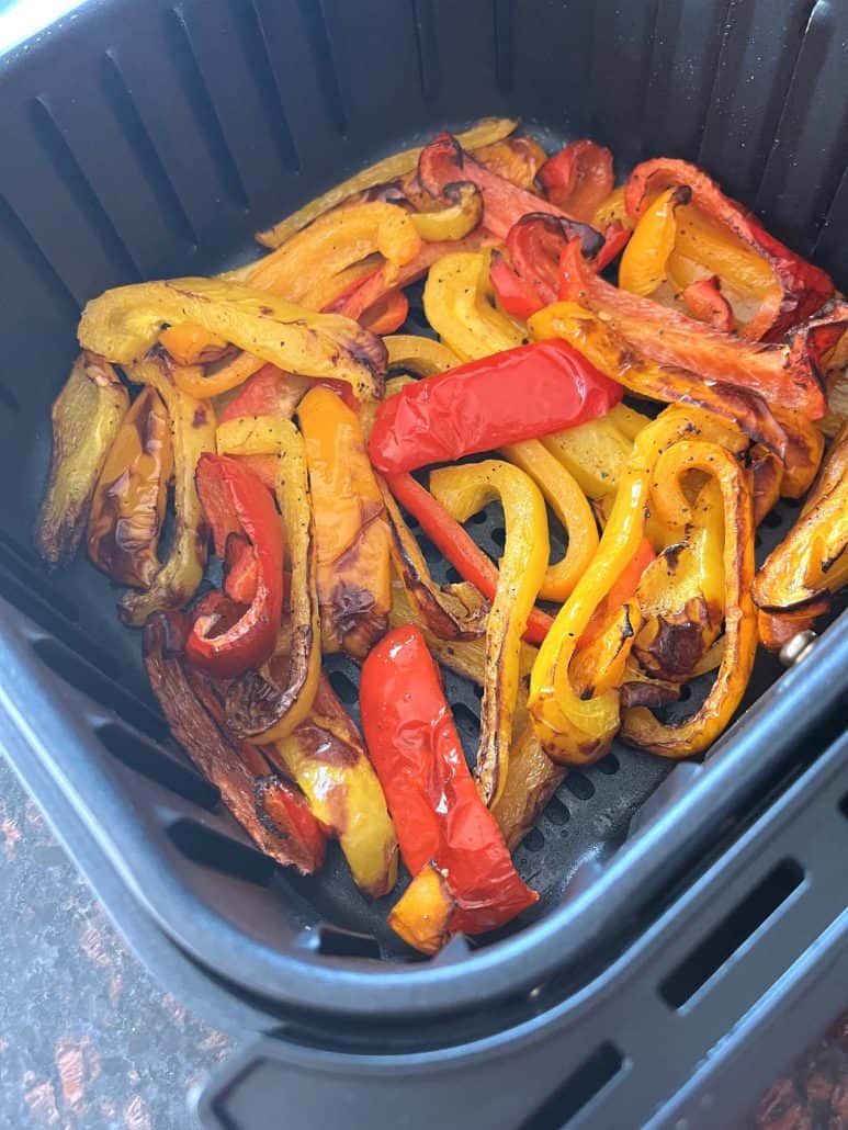 Angled view of air fryer basket filled with roasted tri-color bell peppers—vibrant and caramelized.