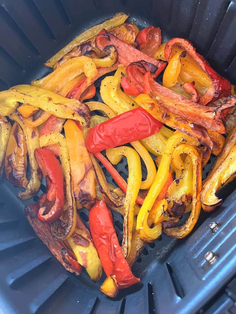 Roasted red, yellow, and orange bell pepper strips in an air fryer basket, showing the perfectly browned edges.