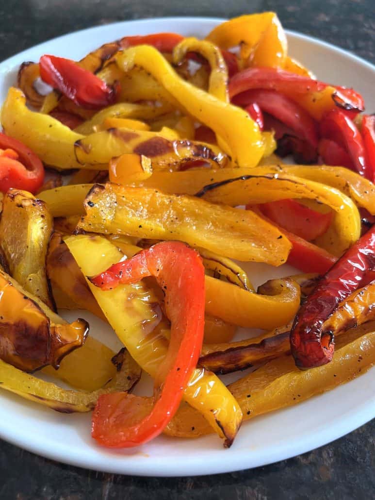 Roasted red, yellow, and orange bell pepper strips on a white plate—vibrant and caramelized.