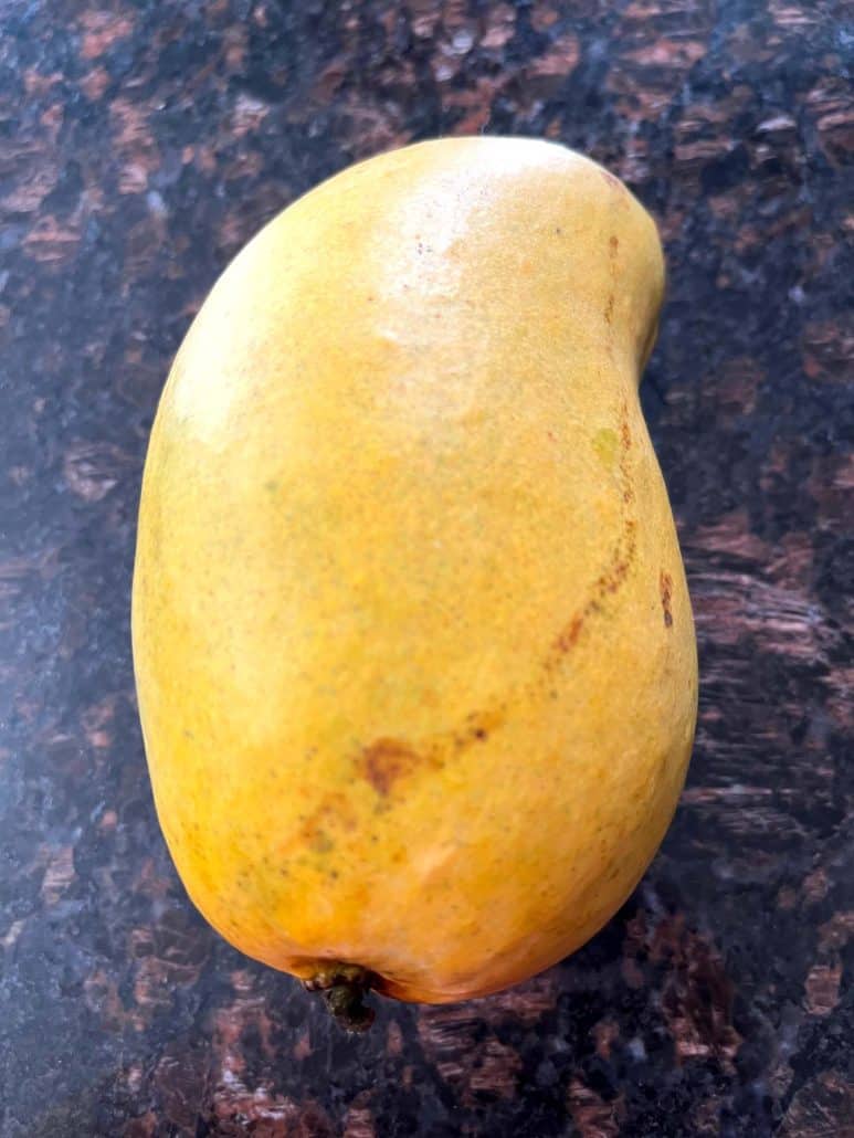 Ripe Philippine Carabao (Manila) mango on a dark kitchen counter, ready to be peeled and sliced using the step-by-step cutting guide.