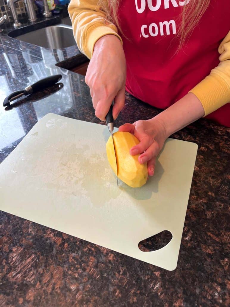 Cutting a peeled Philippine Carabao (Manila) mango vertically on a cutting board to slice around the pit.