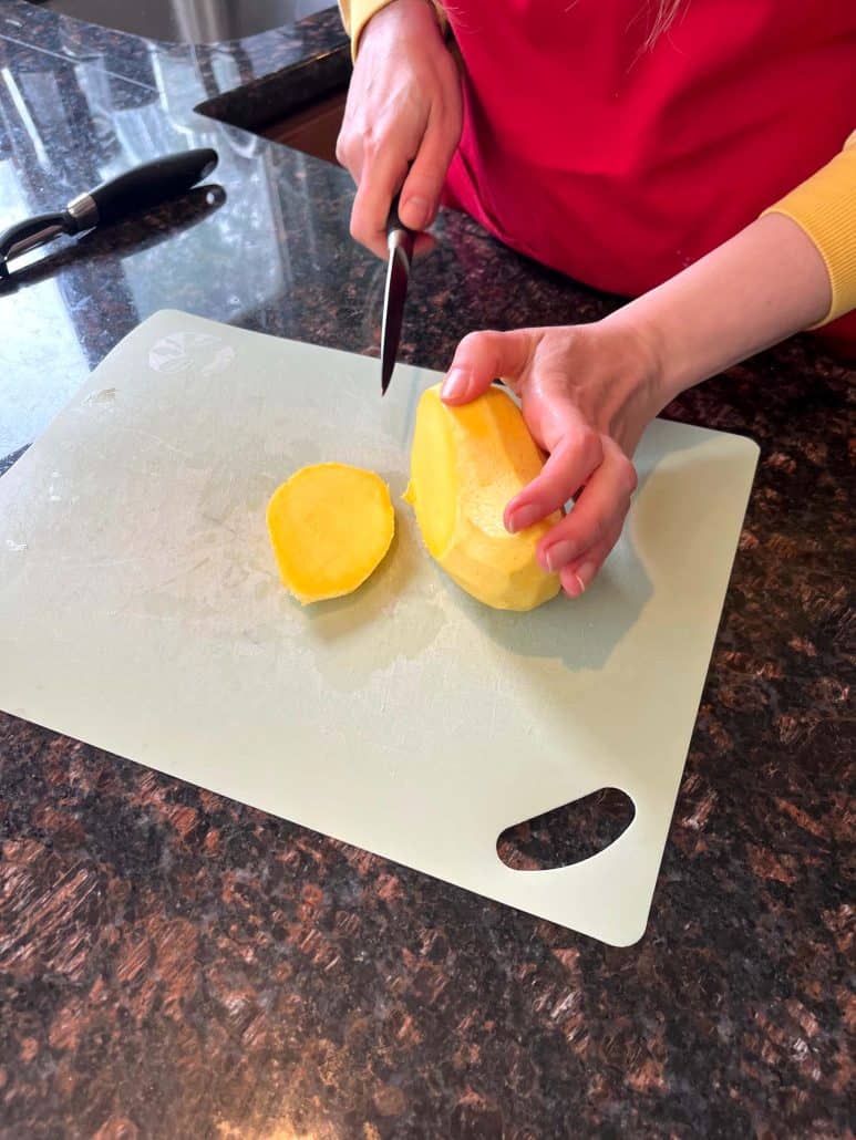 Slicing the cheek off a peeled Philippine Carabao (Manila) mango on a cutting board, showing how to cut around the flat pit.