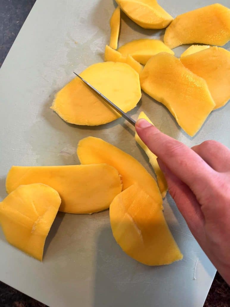 Slicing large mango cheeks into smaller pieces on a cutting board as the final step in preparing a Philippine Carabao (Manila) mango.