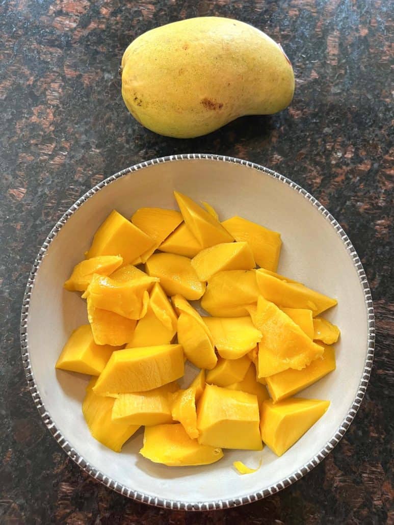 Sliced Philippine Carabao (Manila) mango in a bowl with the uncut mango in the background, showing the result of the cutting method from the guide.