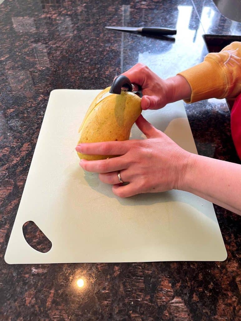 Peeling a Philippine Carabao (Manila) mango on a cutting board, beginning the step-by-step cutting tutorial.