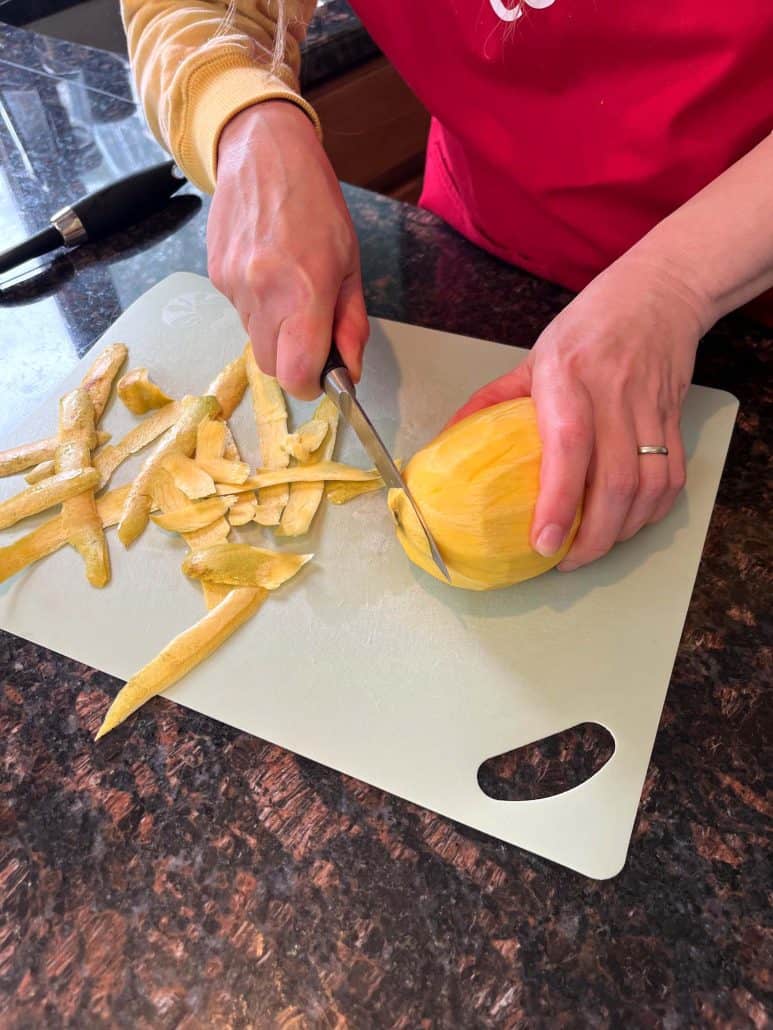 Slicing a peeled Philippine Carabao (Manila) mango on a cutting board, showing the next step after peeling.