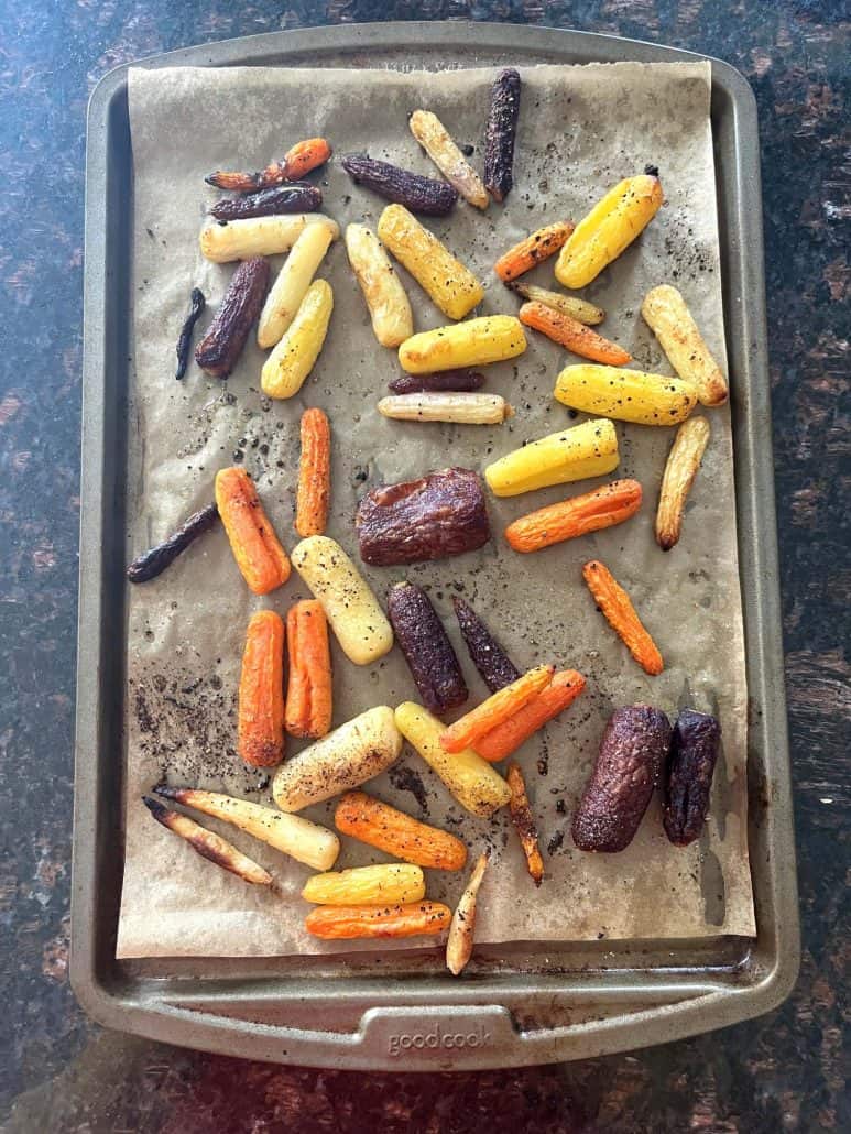 Roasted tri-color baby carrots on a parchment-lined baking sheet, fresh from the oven.