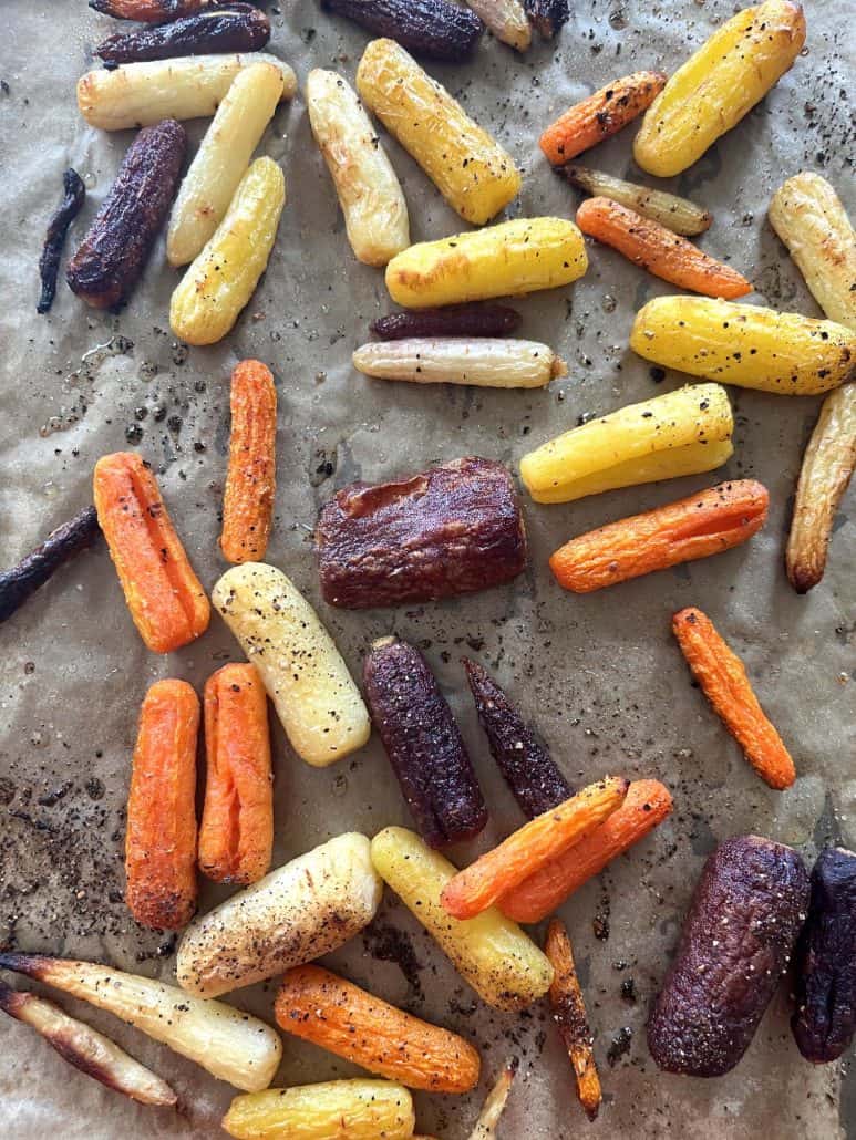 Golden roasted tri-color baby carrots on a baking sheet, highlighting the crisp edges and vibrant colors.
