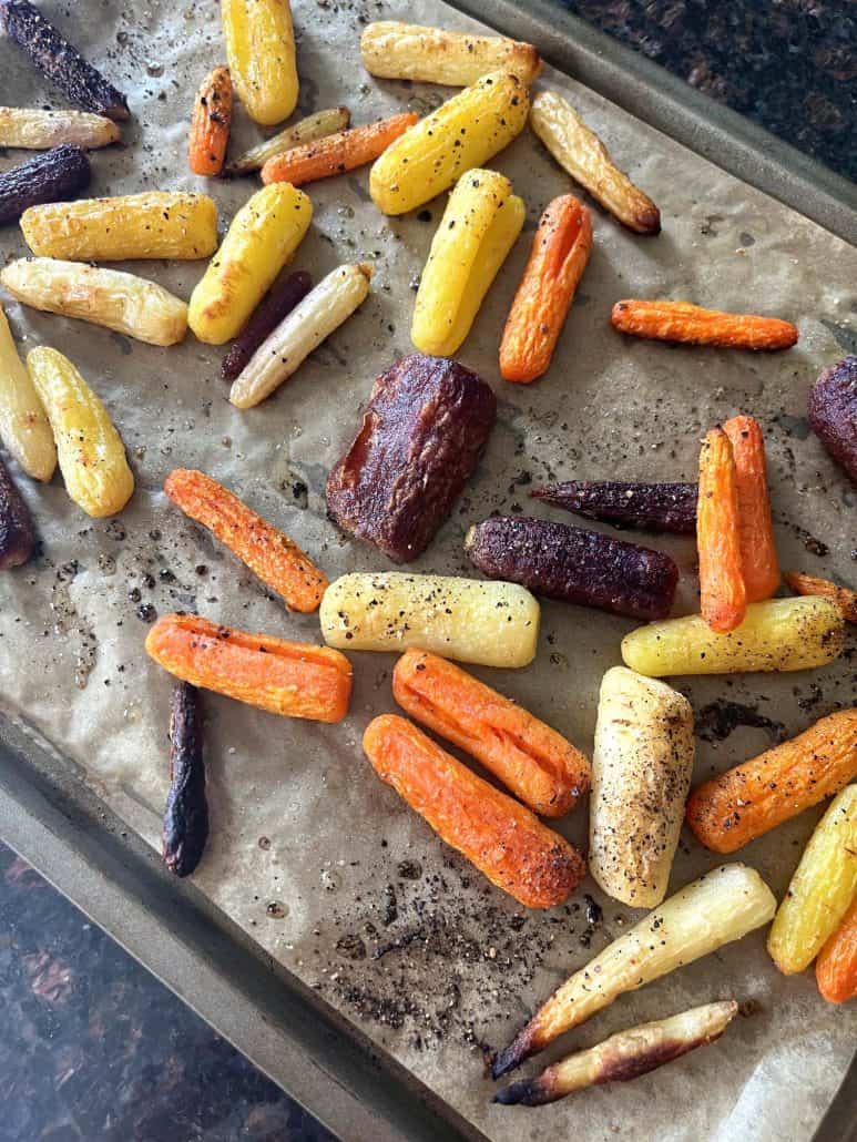 Close-up of roasted tri-color carrots on a parchment-lined baking sheet, showing their golden and crispy edges.