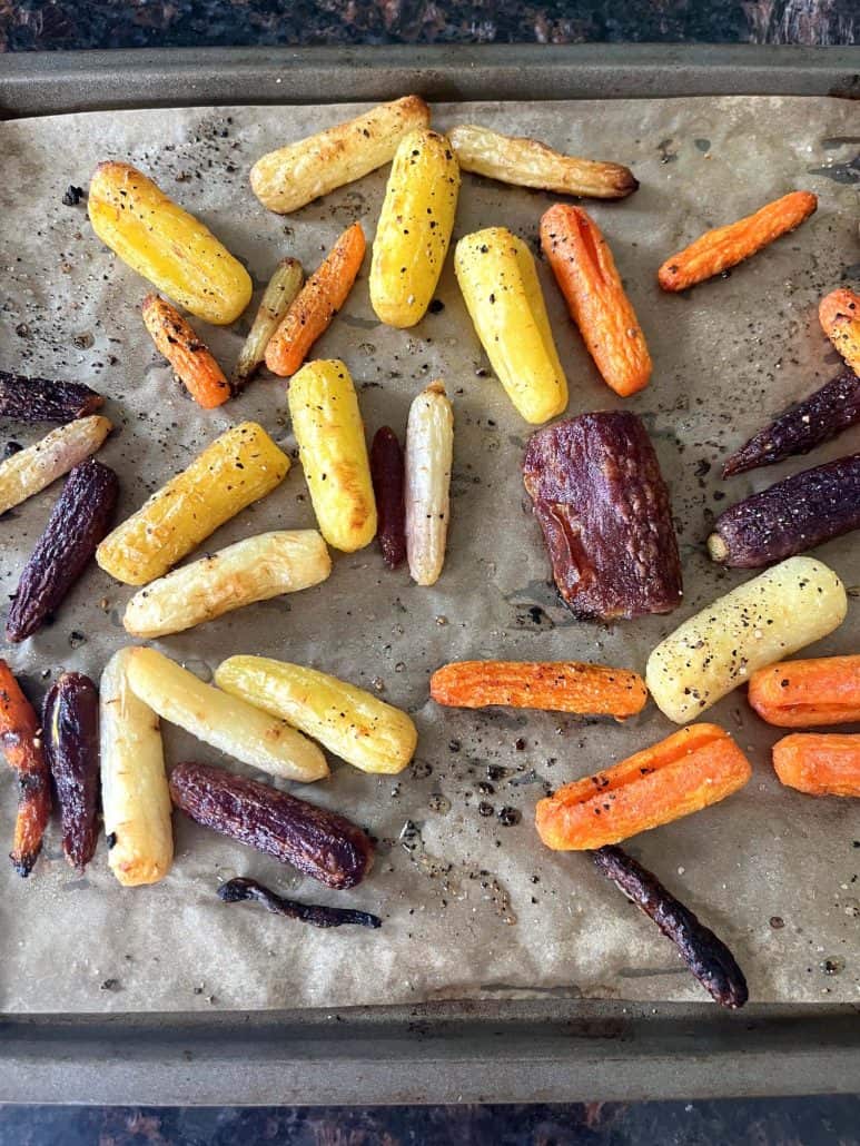 Tri-color baby carrots roasted on a parchment-lined baking sheet, part of the step-by-step process.
