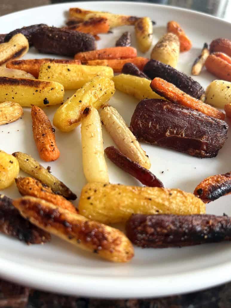 Oven roasted tri-color baby carrots on a white plate, showing caramelized edges.