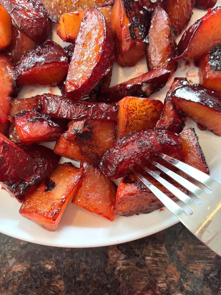 Fork digging into a plate of warm, caramelized sauteed plums, ready to enjoy.