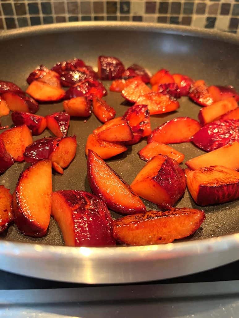 Sliced plums sizzling in a frying pan during the cooking process.