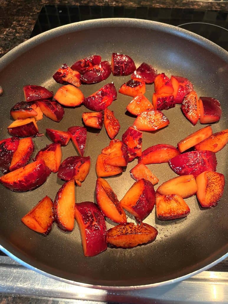 Sliced plums cooking in a nonstick frying pan, the first step in the Sauteed Plums Recipe to caramelize the fruit.
