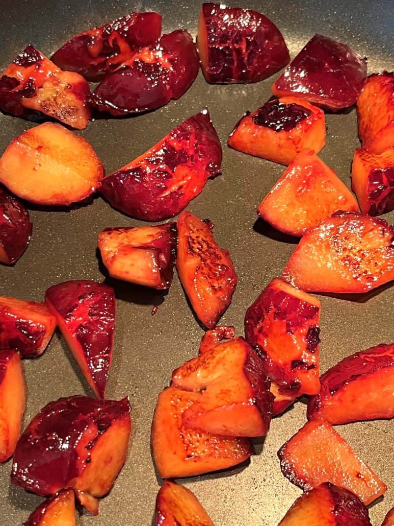 Close-up view of plum slices starting to caramelize in a nonstick pan.