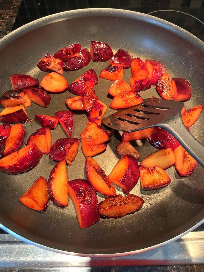 Sliced plums being stirred in a frying pan with a spatula while cooking the Sauteed Plums Recipe on the stovetop.