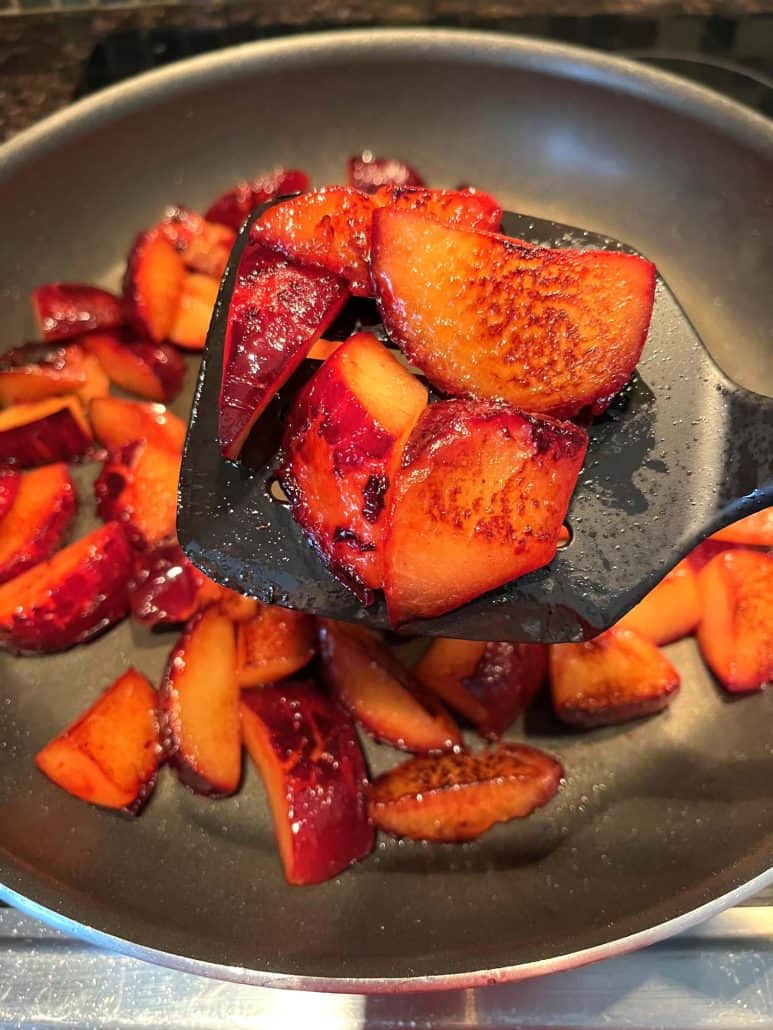 Close-up of caramelized plum slices on a spatula, lifted from the pan during cooking.