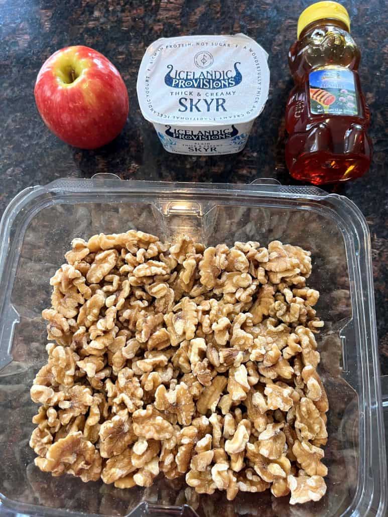 Ingredients for a Skyr bowl with apples and walnuts laid out, including a fresh apple, plain Skyr yogurt, honey, and a container of chopped walnuts—perfect for assembling the no-cook breakfast recipe.