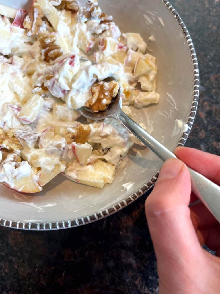 Hand holding a spoon ready to dig into a Skyr bowl with apples and walnuts, highlighting the creamy texture and wholesome ingredients.