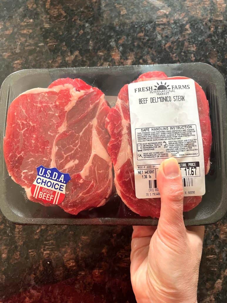 Packaged raw Delmonico steaks being held before air frying, ready for seasoning in this easy steak recipe.